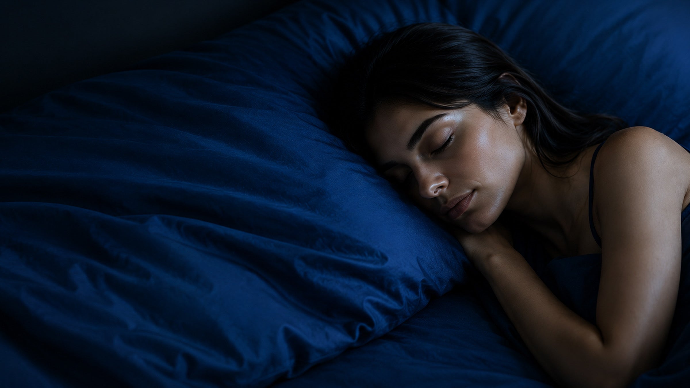 A woman asleep on deep navy bedding in low evening light